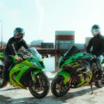 Dua pengendara motor berboncengan di depan kontainer pengiriman, menggambarkan pengiriman motor via ekspedisi kargo