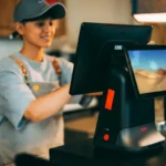 Kasir menggunakan terminal sistem POS modern di toko untuk memproses transaksi penjualan